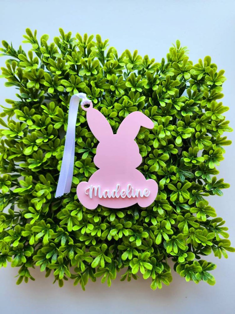 May include: Pink bunny-shaped Easter decoration with the name "Madeline" written in white on the front.