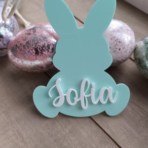 May include: A light blue bunny-shaped Easter ornament with the name "Sofia" written in white on the front.