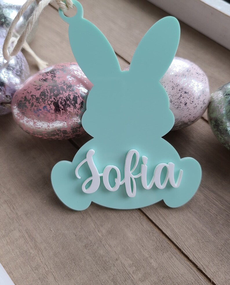May include: A light blue bunny-shaped Easter ornament with the name "Sofia" written in white on the front.