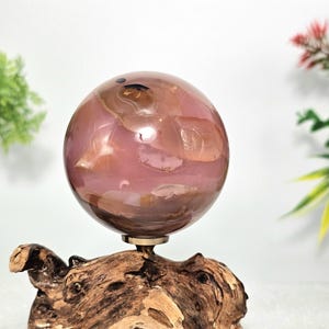 May include: A decorative sphere in shades of pink and brown, mounted on a natural wood base. The sphere has a polished, translucent appearance. The wood base has a unique, organic shape with various textures and colors.
