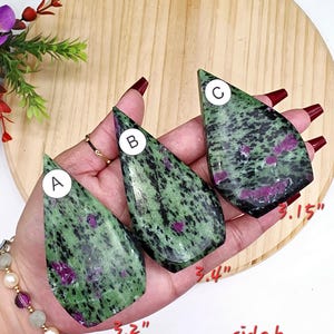 May include: Three teardrop-shaped polished stones labeled A, B, and C, featuring a green and black speckled pattern with magenta inclusions. The stones measure 3.2 inches, 3.4 inches, and 3.15 inches respectively, as indicated by red text labels.