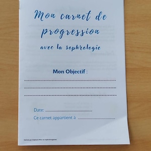 May include: A white booklet with blue cursive text reading "Mon carnet de progression avec la sophrologie." The booklet includes sections for objectives, a date, and owner information. The booklet is on a light brown surface.