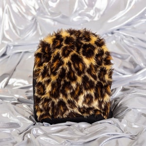May include: A black and brown leopard print faux fur hat. The hat is soft and fluffy and has a black band around the bottom.
