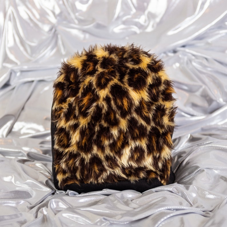 May include: A black and brown leopard print faux fur hat. The hat is soft and fluffy and has a black band around the bottom.