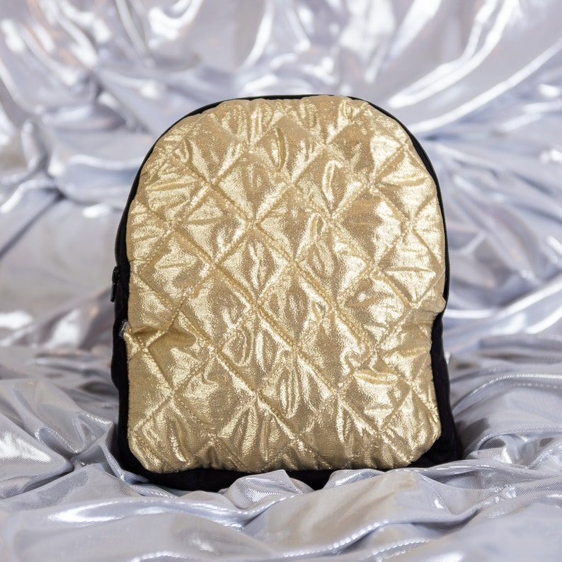 May include: A black quilted backpack with a gold metallic finish. The backpack has a diamond-shaped quilted pattern.