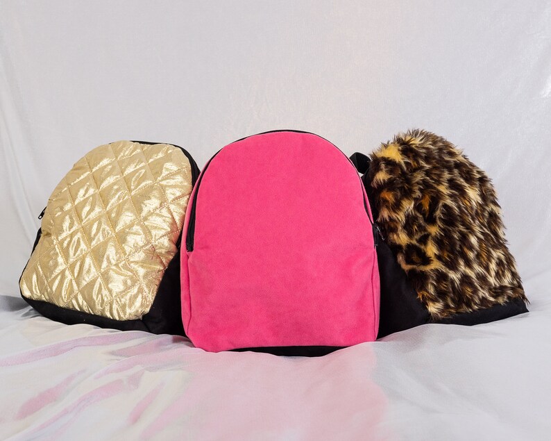 May include: Three small backpacks in different colors and patterns. The backpack on the left is gold with a quilted design. The middle backpack is pink. The backpack on the right is black with a brown and black animal print.