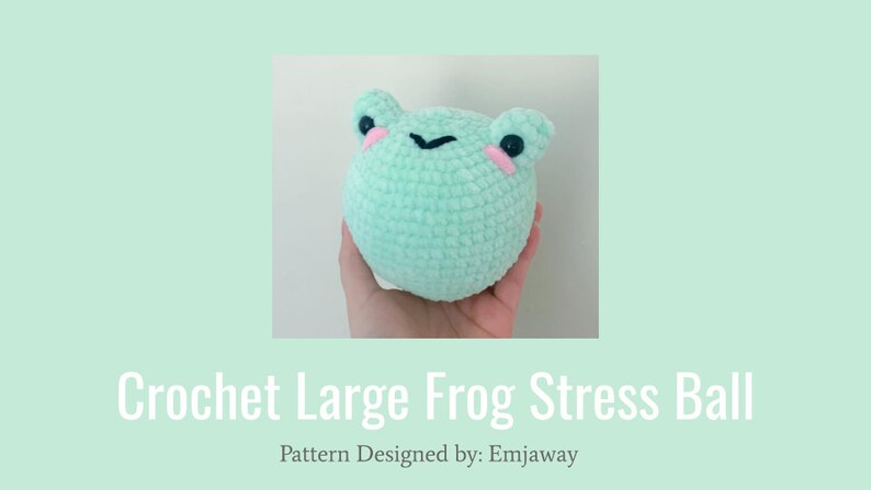 May include: A light green crocheted frog stress ball with black eyes and pink cheeks. The ball is being held in a hand.