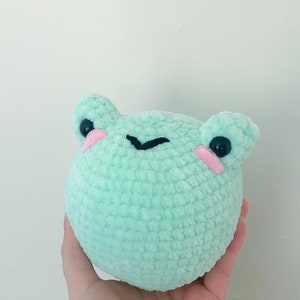May include: A light green crocheted frog plush toy with black eyes and pink cheeks.