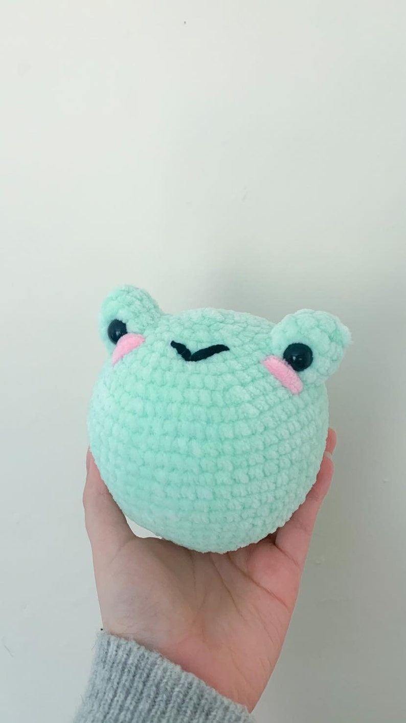 May include: A light green crocheted frog plush toy with black eyes and pink cheeks.
