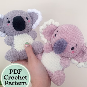 May include: Two crocheted koala plushies, one gray and one pink, with white fur accents. The plushies have black eyes and noses, and pink cheeks. The plushies are held in a hand, and a sign that says "PDF Crochet Pattern" is in the foreground.