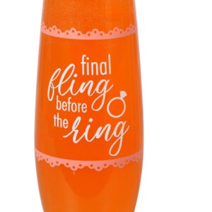 May include: A clear glass champagne flute with a pink and white design. The glass has the text "final fling before the ring" printed on it.