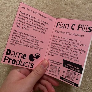 Puede incluir: Se muestra un folleto rosa con los t&iacute;tulos "Dame Products" y "Plan C Pills". El folleto proporciona informaci&oacute;n sobre productos de bienestar sexual y acceso a p&iacute;ldoras abortivas. El texto incluye direcciones de sitios web y c&oacute;digos QR.