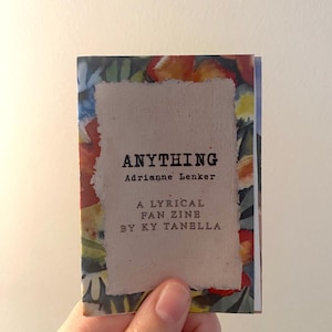 May include: A small, handmade zine titled "ANYTHING" by Adrianne Lenker and Ky Tanella. The cover features a torn, textured paper with the title in bold black letters. The zine is surrounded by a colorful floral watercolor design.