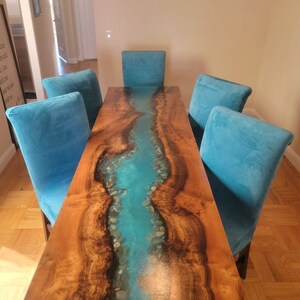 May include: A wooden dining table with a turquoise epoxy river running down the center. The table is surrounded by four teal blue chairs.