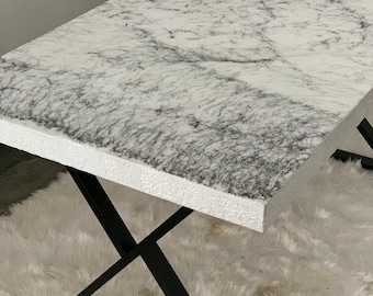 May include: White marble top coffee table with a black metal X-shaped base. The table is sitting on a white fluffy rug.
