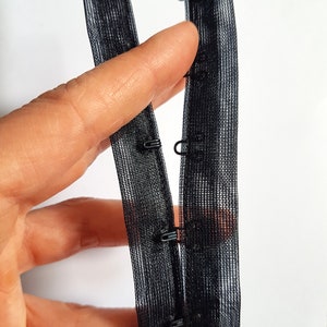 May include: Black elastic bra strap with metal hooks and eyes. The strap is made of a mesh material.