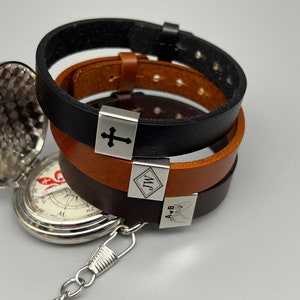 May include: Three leather bracelets with silver metal charms. The charms have the words "J.M." and "A & B" engraved on them, and one charm has a cross engraved on it.