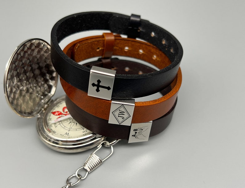 May include: Three leather bracelets with silver metal charms. The charms have the words "J.M." and "A & B" engraved on them, and one charm has a cross engraved on it.