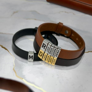 May include: Two leather bracelets with personalized name tags. The bracelets are brown and black leather. The name tags are silver with gold lettering. The names on the tags are: R, D, Lori, Lily, Juan, Rose, Amy, Laura, Lisa, and Anna.