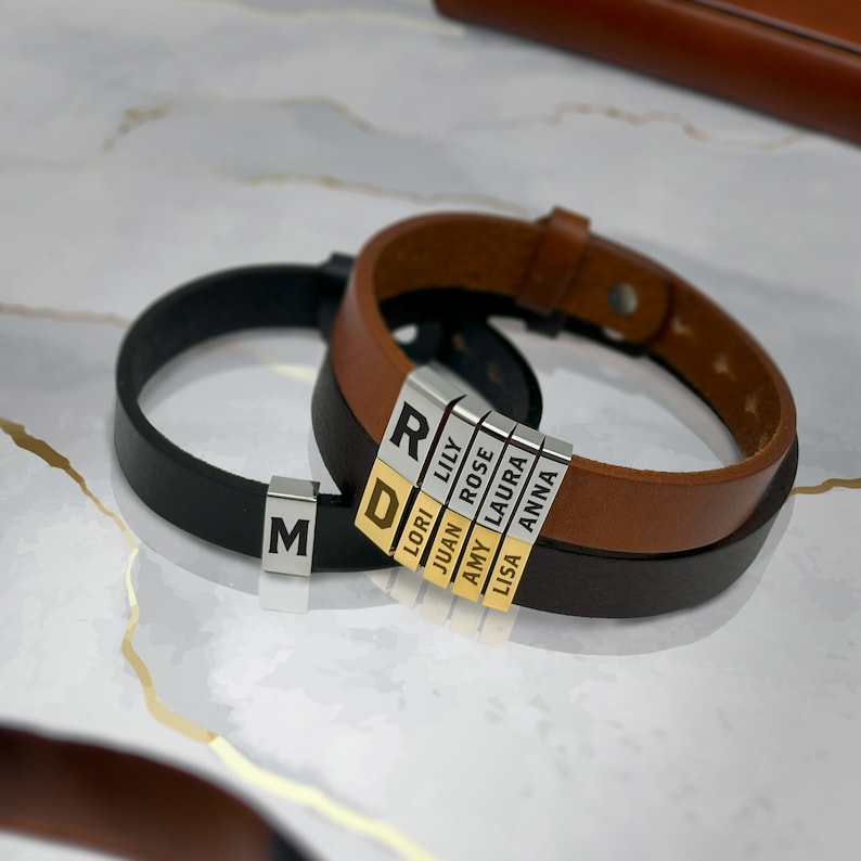 May include: Two leather bracelets with personalized name tags. The bracelets are brown and black leather. The name tags are silver with gold lettering. The names on the tags are: R, D, Lori, Lily, Juan, Rose, Amy, Laura, Lisa, and Anna.