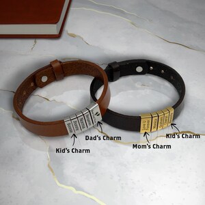 May include: Two leather bracelets with personalized charms. The brown bracelet has silver charms with the names Bonnie, Jhonny, Norma, Benjamin, and "Best Dad Ever". The black bracelet has gold charms with the words "Love U", "Forever", Monica, Graham, Cheryl, and Beverly.