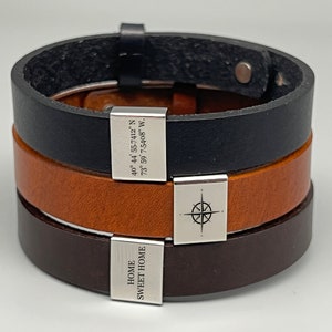 May include: Three leather bracelets with silver charms. The top bracelet is black leather with a silver charm that reads "40&deg; 44' 55-7412" N 73&deg; 59' 7.5408" W.". The middle bracelet is brown leather with a silver compass charm. The bottom bracelet is dark brown leather with a silver charm that reads "HOME SWEET HOME".
