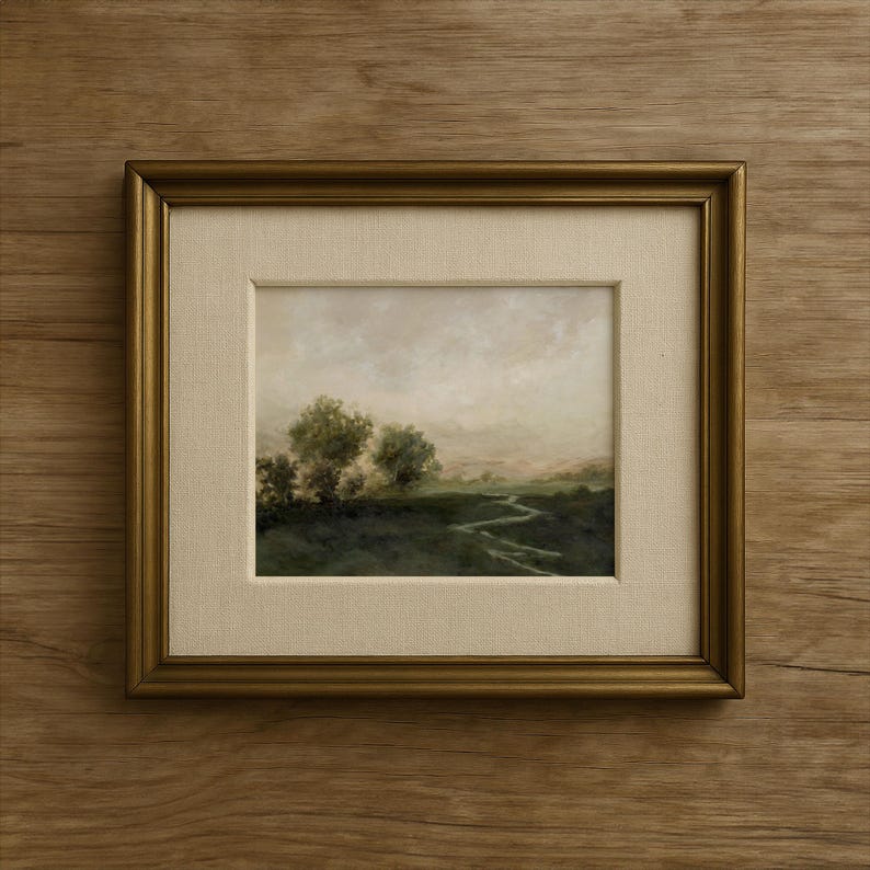 May include: Framed landscape painting featuring a serene outdoor scene. The artwork depicts a winding path through a green field, with trees and a cloudy sky. The painting is set within a gold-colored frame with a cream-colored mat.