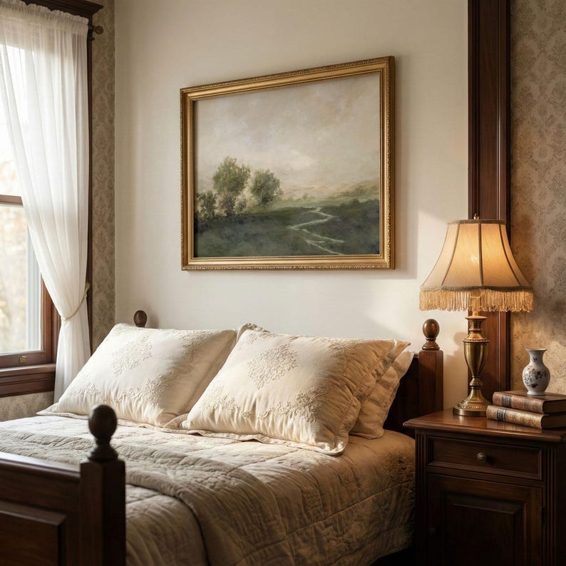 May include: A bedroom scene featuring a bed with cream-colored bedding and embroidered pillows. A landscape painting in a gold frame hangs above the bed. A lamp with a fringed shade sits on a wooden nightstand.