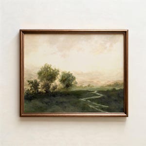 May include: A framed landscape painting with a bronze-colored frame. The artwork depicts a serene, misty scene with trees, a winding stream, and a soft, neutral sky. The color palette is dominated by greens, browns, and creams.