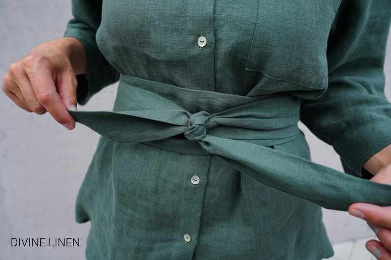 May include: A green linen shirt with a matching green linen belt tied around the waist. The shirt has a button-up front and long sleeves.