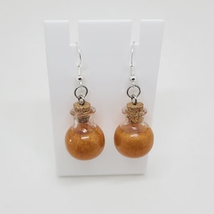 May include: A pair of gold glitter potion bottle earrings with cork stoppers and silver hooks.