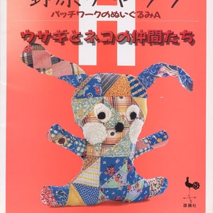 Könnte beinhalten: Ein Buchcover mit rotem Hintergrund und dem Titel "野原チャック パッチワークのぬいぐるみA ウサギとネコの仲間たち" in Japanisch. Das Cover zeigt ein Patchwork-Stofftierkaninchen mit weißem Fell um das Gesicht.
