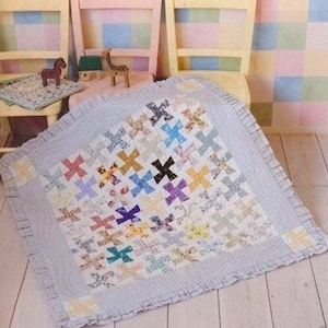 Könnte beinhalten: Eine blaue und weiße Patchwork-Decke mit einem Rüschenrand. Die Decke besteht aus kleinen Stoffquadraten mit verschiedenen Mustern und Farben, darunter Rosa, Lila, Gelb und Grün. Die Decke liegt auf einem Holzboden.