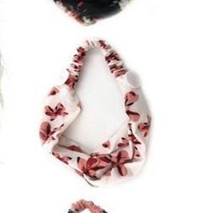 Könnte beinhalten: Drei Blumenmuster-Stirnbänder. Das erste Stirnband ist schwarz mit rosa und weißen Blumen. Das zweite Stirnband ist weiß mit rosa Blumen. Das dritte Stirnband ist rosa mit weißen und grünen Blumen. Jedes Stirnband hat auf jeder Seite einen Knopf.