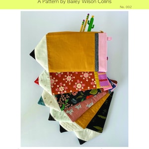 Puede incluir: Un conjunto de seis estuches para l&aacute;pices en diferentes telas coloridas, cada uno con forma de l&aacute;piz. Los estuches est&aacute;n apilados uno encima del otro, con el estuche superior de color amarillo mostaza. Los estuches est&aacute;n hechos de tela de algod&oacute;n y tienen cierre de cremallera. El texto "School Days Pencil Pouch" y "No. 002" es visible en la parte superior de la imagen.