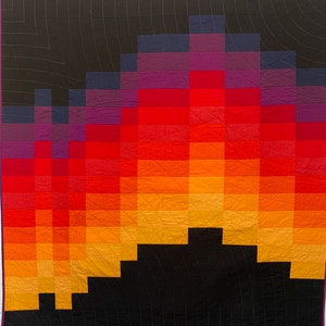 May include: A quilt with a pixelated design of a sunset in shades of purple, red, orange, and yellow. The sunset is set against a black background.