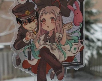 May include: A clear sticker featuring two anime characters. The female character has long green hair and is wearing a white dress with a black bow. The male character has short black hair and is wearing a black uniform with a red hat. The sticker is set against a snowy background.