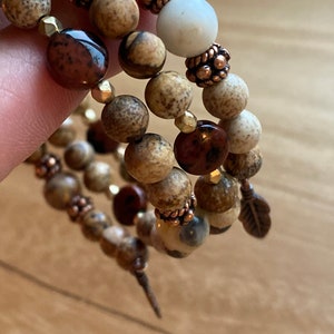 May include: A multi-strand bracelet with brown and white beads, copper accents, and a small feather charm.