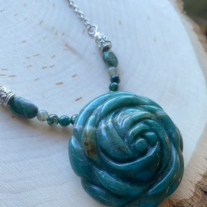 May include: A green jade rose pendant necklace with a silver chain and beads. The rose is carved from a single piece of jade and has a natural, organic look.