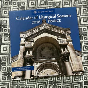 May include: A calendar titled "Calendar of Liturgical Seasons 2026 FRANCE" featuring a photograph of a stone church with arched doorways and columns. The calendar is from "BEAUTY FIRST FILMS" and includes the text "New/Revised Julian".