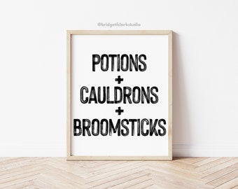 May include: A framed print with the words "POTIONS + CAULDRONS + BROOMSTICKS" in bold, black letters on a white background. The frame is a light wood color. The print is displayed on a white wall above a wooden floor.