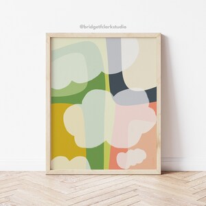 May include: Abstract art print with a colorful design featuring green, yellow, pink, blue, and white shapes. The print is framed in a light wood frame.