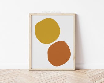 May include: A digital print featuring two abstract shapes, one yellow and one orange, on a white background. The print is framed in a light wood frame.