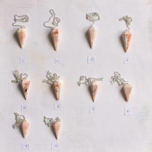 Op de afbeelding: Tien roze en witte kristallen pendels met zilveren kettingen. De pendels zijn genummerd van 1 tot en met 10.