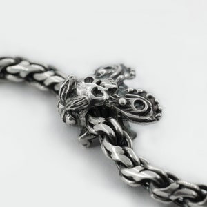 May include: A silver charm bracelet with a detailed skull and butterfly charm. The charm is attached to a silver chain with a braided design.