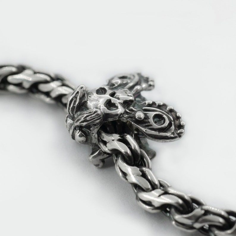 May include: A silver charm bracelet with a detailed skull and butterfly charm. The charm is attached to a silver chain with a braided design.