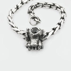 May include: A silver bracelet with a black gemstone spider charm. The bracelet has a braided chain design.