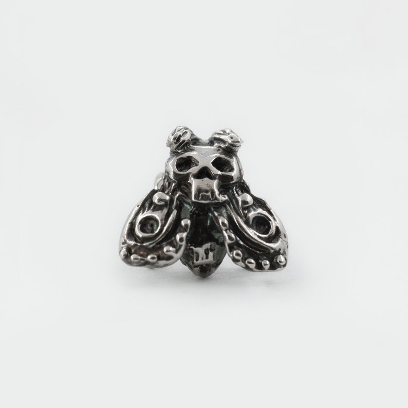 May include: A silver skull moth charm with intricate details. The moth has a skull-shaped head and detailed wings.
