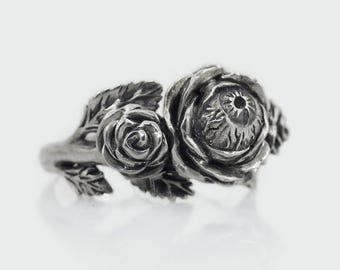 May include: A silver ring with two roses, one of which has an eye in the center.