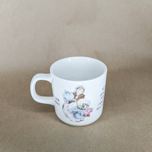 May include: White ceramic mug with a curved handle. The mug features a colorful illustration of a child with a dog and text. The text on the mug reads "All the little ducks came down to the ferry".